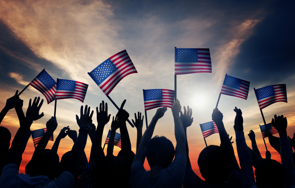 Group,Of,People,Waving,American,Flags,In,Back,Lit